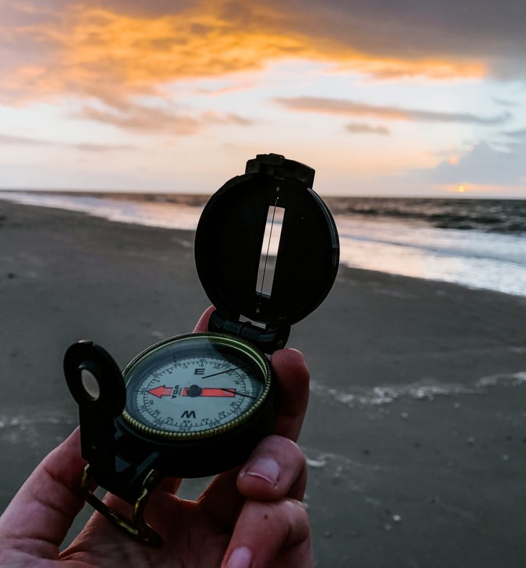 En hånd holder et kompass på en strand med havet i bakgrunnen