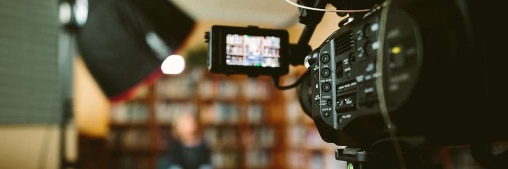Filmkamera som filmen en person som sitter med en bokhylle i bakgrunnen.