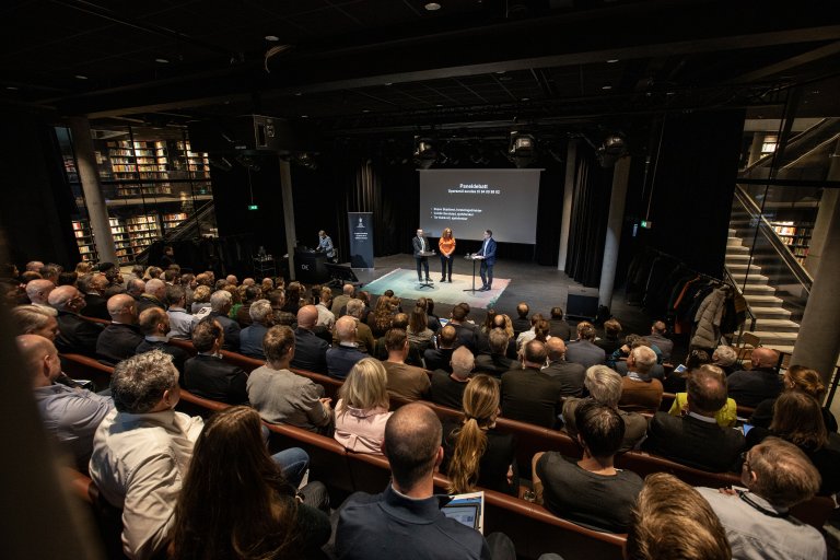 en sal sett bakfra full av folk som sitter og hører på foredrag