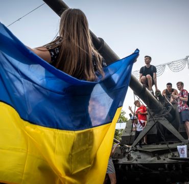 Jente holder Ukrainsk flagg. Unger og tenåringer klatrer på en beslaglagt Russisk stridsvogn som er utstilt på gaten i Kiev.