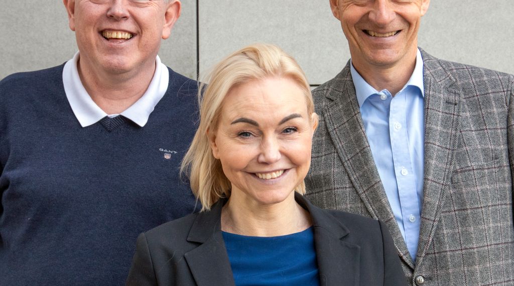 Portrett av tre forskewre foran en grå vegg.