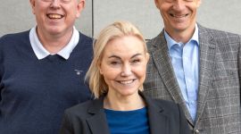 Portrett av tre forskewre foran en grå vegg.