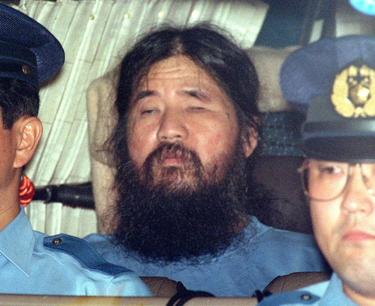 Shoko Asahara - ustelt mann mellom to politifolk i en politibil.