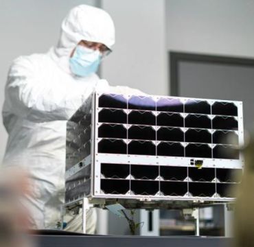 en mann i hvit drakt står bak en satellitt