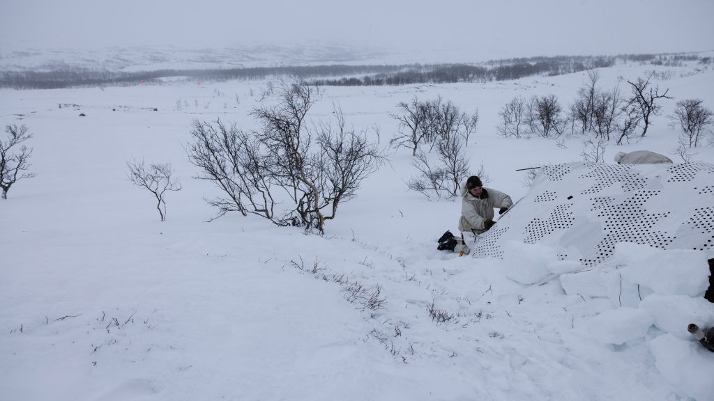 Bilde fra Halkavarre skytefelt i Finnmark. En svensk soldat gjør klar telt på en observasjonspost. Snø, vidde og busker i bakgrunnen.