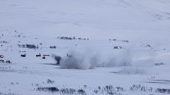 Snø og vidde. Eksplosjon fra et artillerinedslag. Grå røyk og snøsprut.