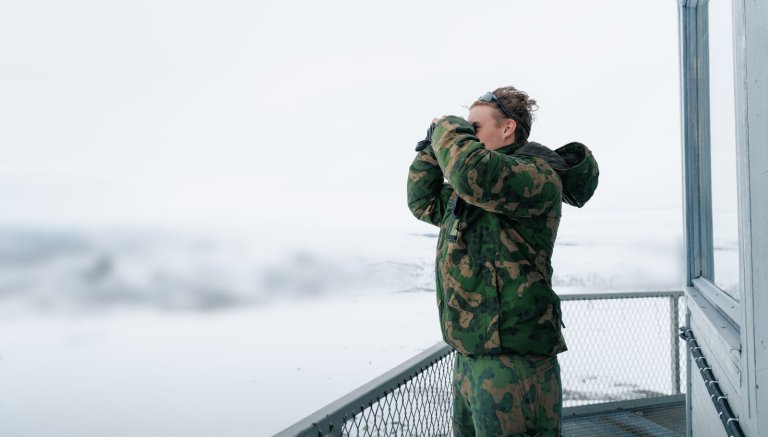 Soldat med kikkert i grønn uniform i vinterlandskap.