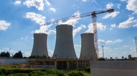 Tre gigantiske kjøletårn. En heisekran. Sol. Utendørs. Blå himmel.