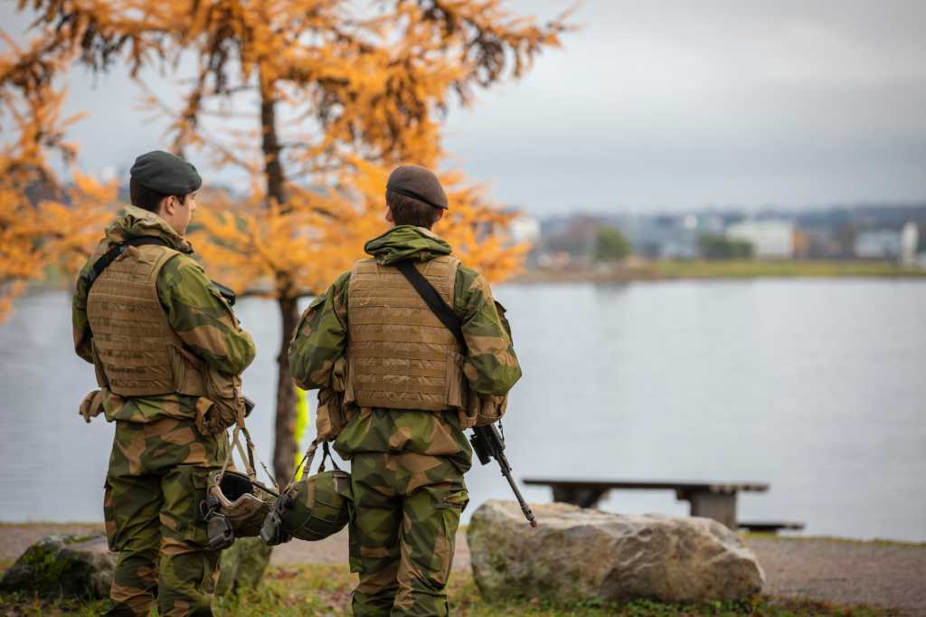 to soldater står med ryggen til og ser utover et vann. Det er høstfarger på trærne.