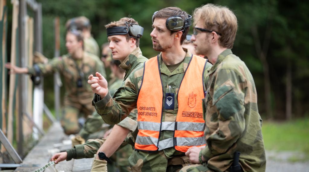Soldater i kamuflasjeuniform på øvelse. En elev og en instruktør står og ser på noe og diskuterer.