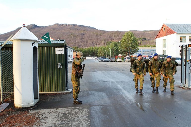 Soldater på vei ut porten på Maukstadmoen leir. En vaktsoldat hilser.