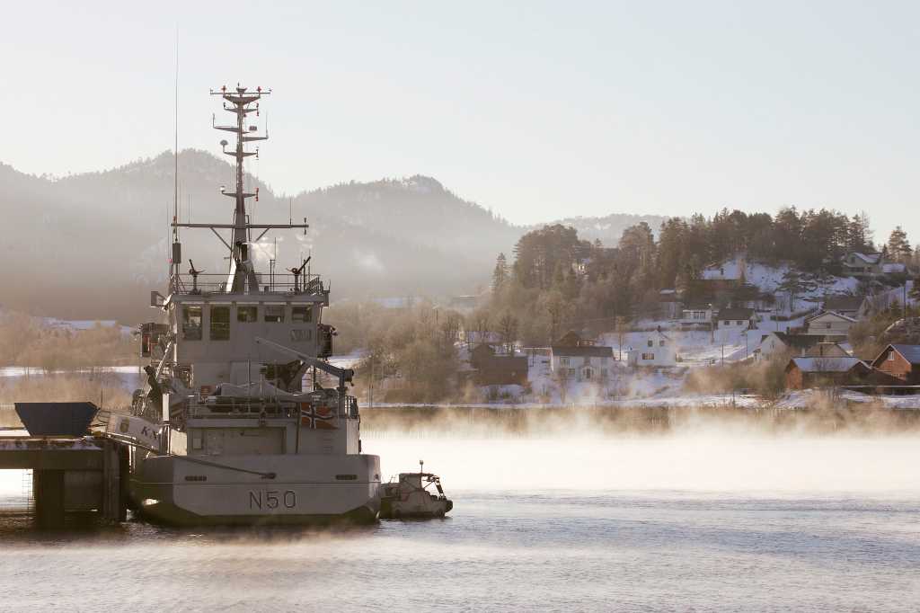 militært fartøy ligger til kai. morgendis og dap på vinterhavet rundt