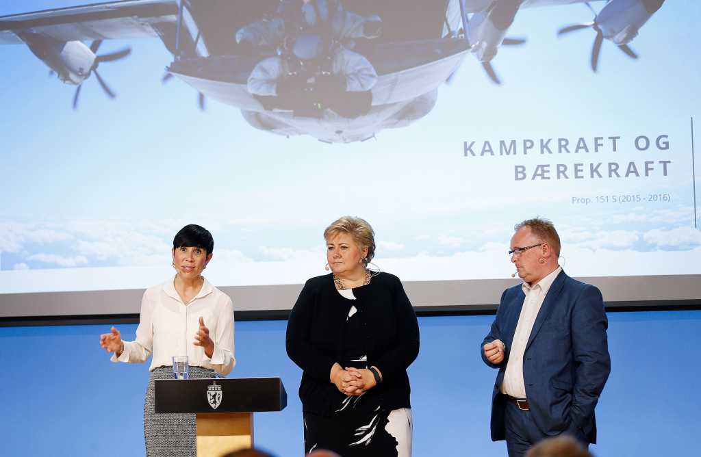 Tre politikere på scenen. Erna Solberg i blåsvart kjole i midten.