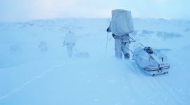Soldater i hvite kamuflasjedrakter som drar pulk på fjellet i dårlig vær.