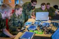 unge soldater i uniform sitter rundt et bord med mye teknologisk utstyr