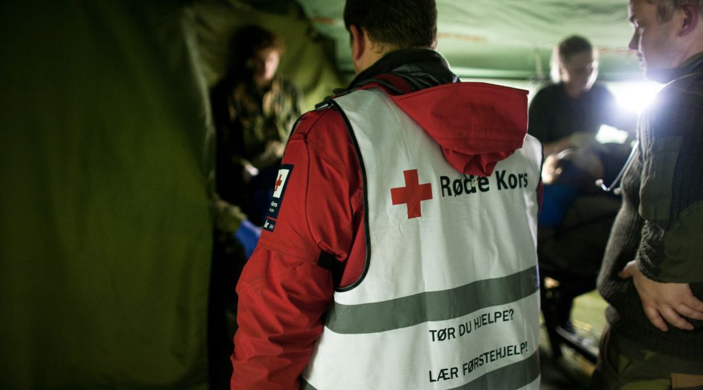 inne i et militært telt. vi ser tyggen på en med vest fra røde kors i fokus og annet militært personell rundt