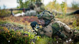 soldat i kamuflasje ligger i norsk lyng og speider med kikkert