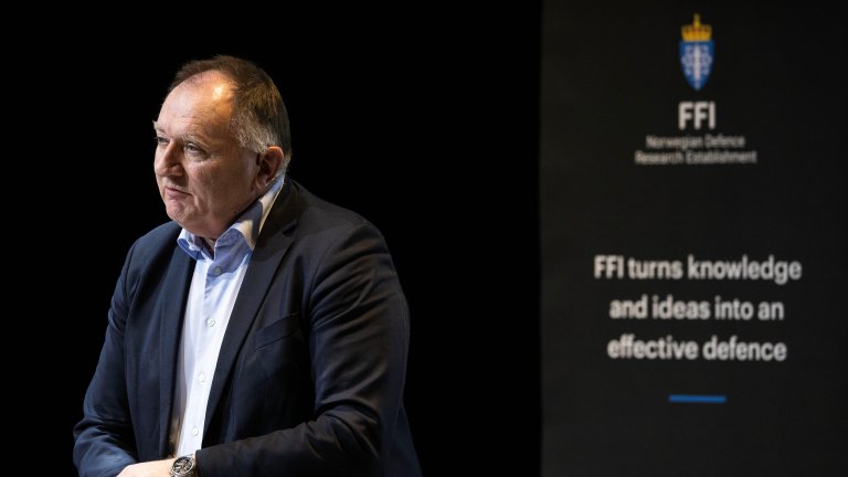 En forsker står og snakker. I bakgrunnen en rollup med FFIs logo.