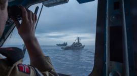 En soldat bruker kikkerten og ser to marinefartøy foran seg.