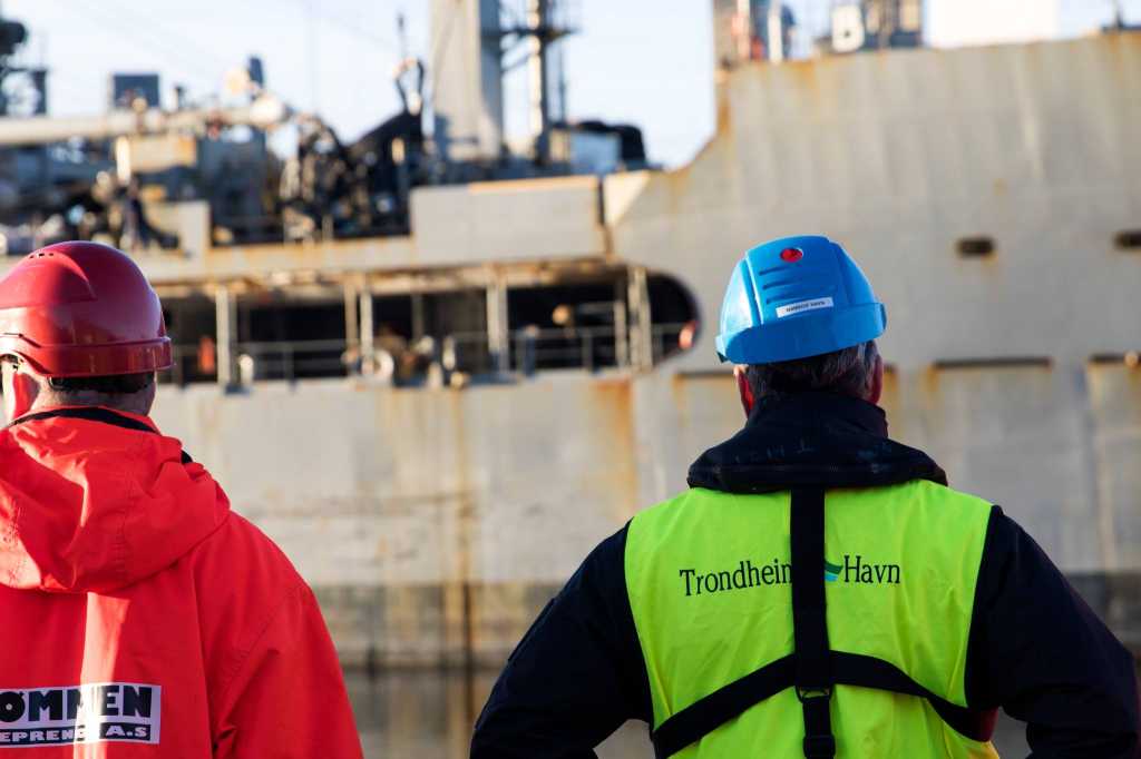 et militært fartøy i en havn med sivile med ryggen til kamera