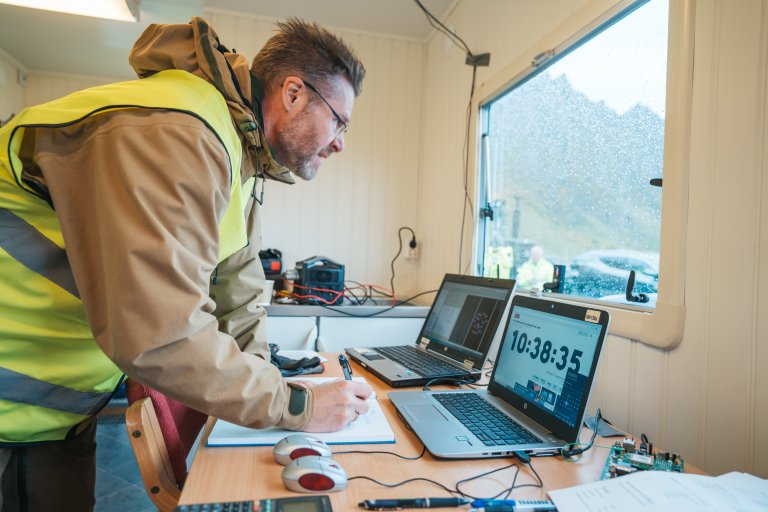 Forsker Anders Rødningsby står med refleksvest inne i en brakke, foran en PC skjerm. Utenfor vinduet ser vi fjellene på Andøya.