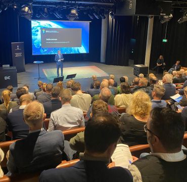 Bakhoder av folk i konferansesal og en mann i dress på scenen