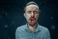 Mann nyser, hoster eller roper mens det spruter dråper ut av munnen hans.