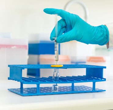 en hånd med hanske i et laboratorium tar noe i et reagensrør 