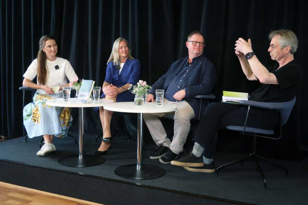 Fire personer sitter på scenen bak to små, runde bord. To kvinner til venstre og to menn til høyre.