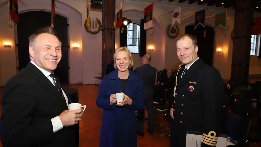 To menn og ei kvinne drikk kaffe. Ein tredje person til høgre i militæruniform.