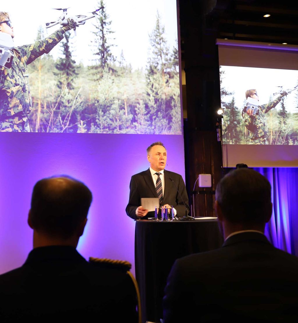 Tore O. Sandvik på på talerstolen. Presentasjonen i bakgrunnen viser en soldat med en drone.