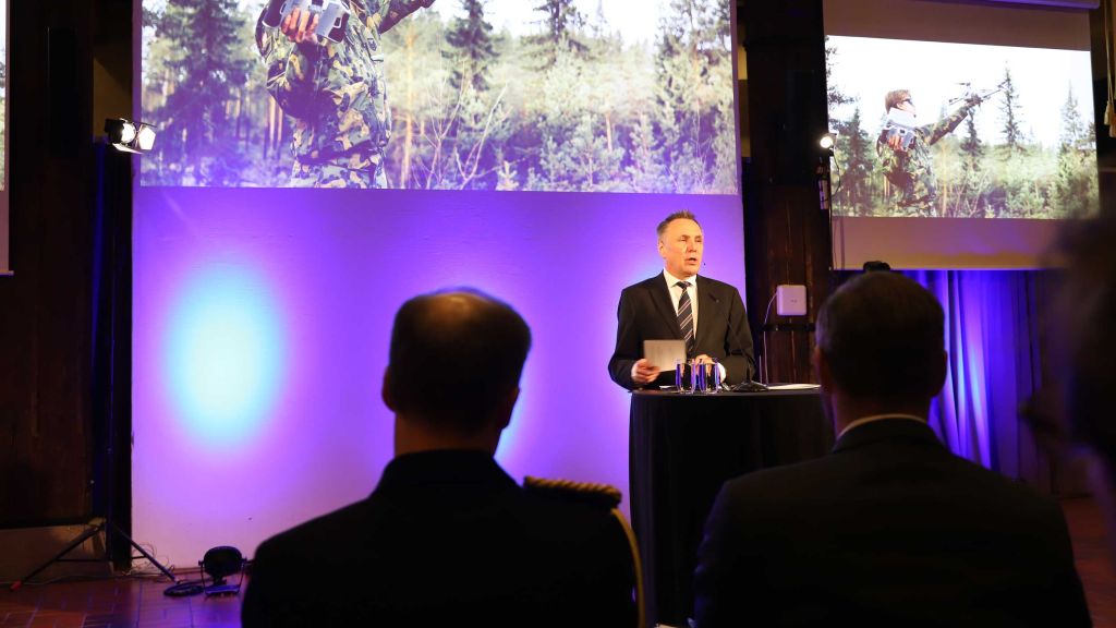 Tore O. Sandvik på på talerstolen. Presentasjonen i bakgrunnen viser en soldat med en drone.