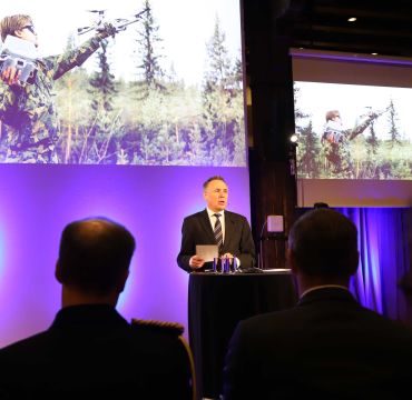 Tore O. Sandvik på på talerstolen. Presentasjonen i bakgrunnen viser en soldat med en drone.