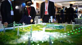 Tre personer ved en installasjon som viser noen strømmaster og det som trolig er en kraftstasjon eller trafo.