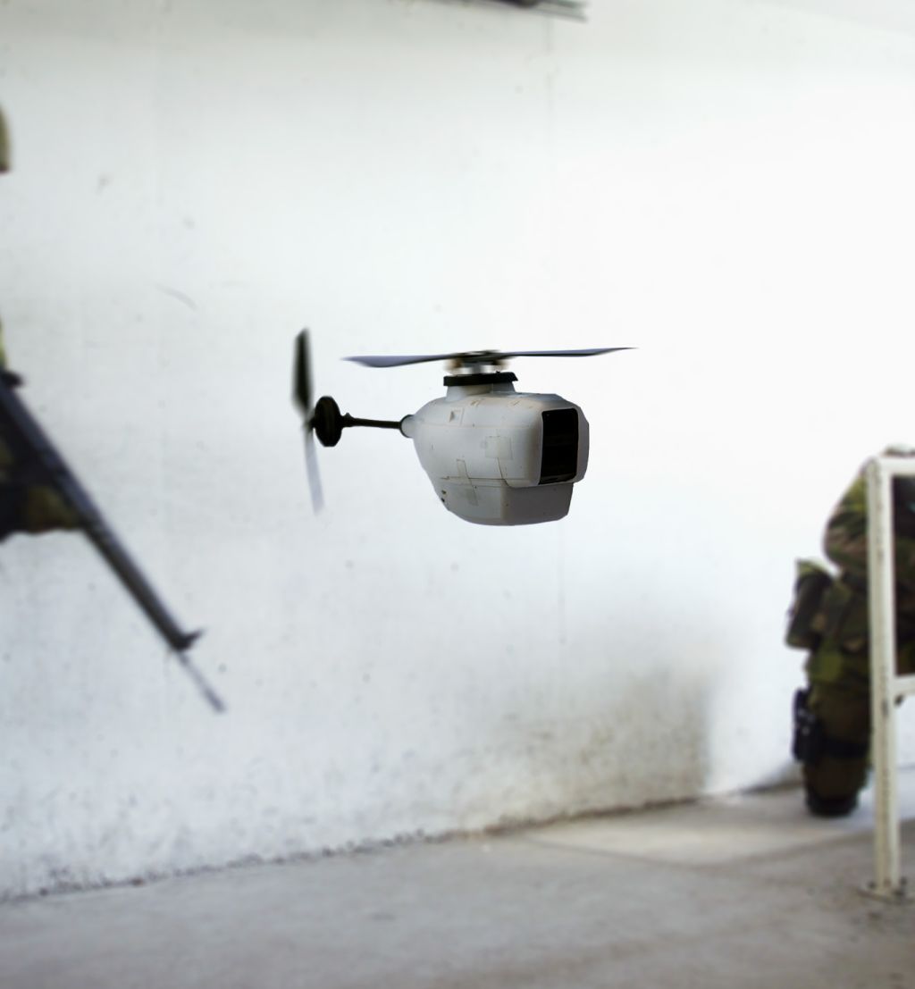 Liten drone i forgrunn, soldat med våpen i bakgrunn. Foto