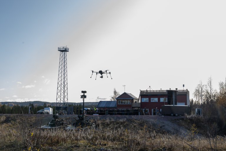 BIlde fra teknologidemonstrasjonen LandX 2023. En drone tar av i forgrunnen. I bakgrunnen ser vi publikum, røde bygninger og en stor 5G-mast.