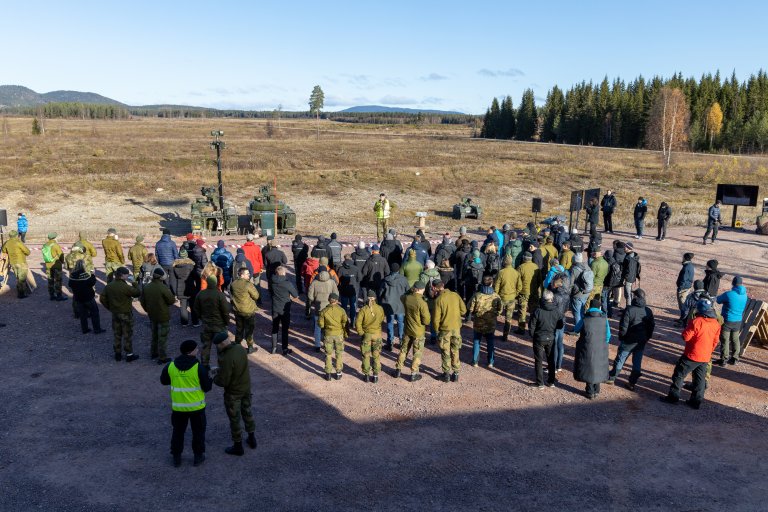 Oversiktsbilde fra teknologidemonstrasjonen LandX23. Publikum står med ryggen til på en grusplass. I bakgrunne ser vi en skytebane og flere militære kjøretøyer.