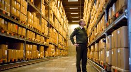 en mann står inne på et lager og ser på hyller med brune pappesker