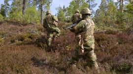 Tre bevæpnede soldater går i lyngen på vei oppover en ås.