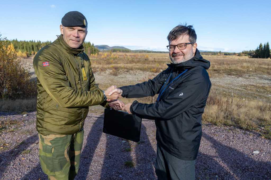 En offiser og en utvikler fra industrien håndhilser. Utendørs. Høst. Skytefelt.