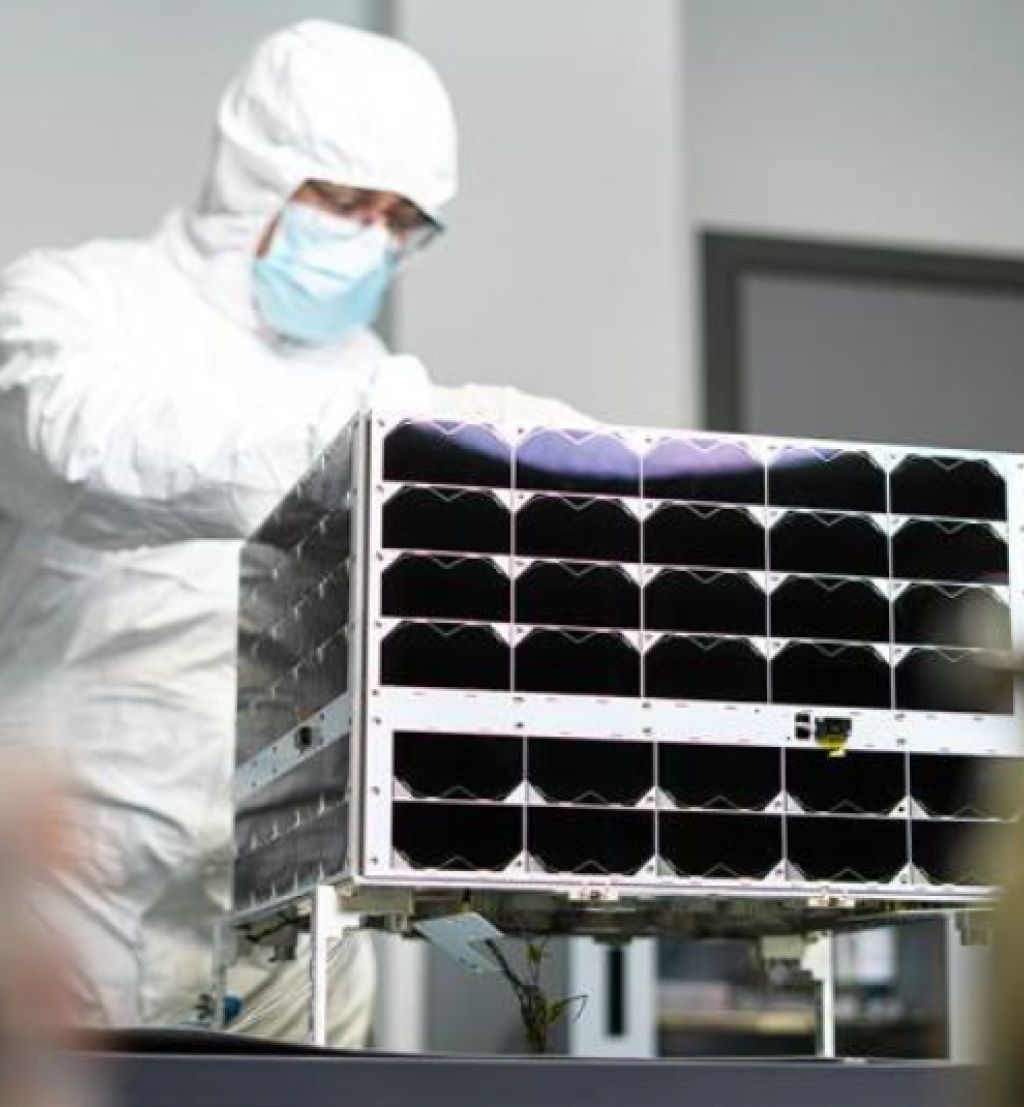 en mann i hvit drakt står bak en satellitt