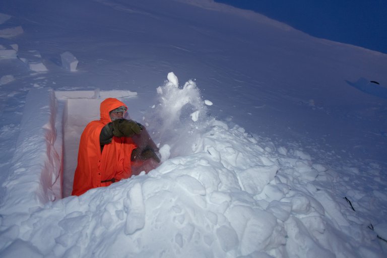 Mann i orange poncho graver snøhule.