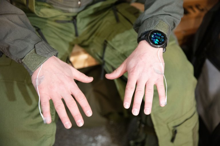 En person i militære klær holder frem hendene. Han har temperaturmåler festet på begge lillefingrene.