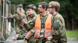 Soldater i kamuflasjeuniform på øvelse. En elev og en instruktør står og ser på noe og diskuterer.