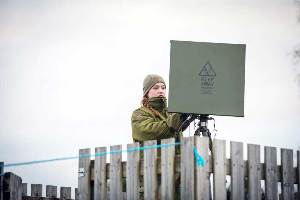 En soldat i grønn uniform setter opp en grønn, kvadratisk antenne.