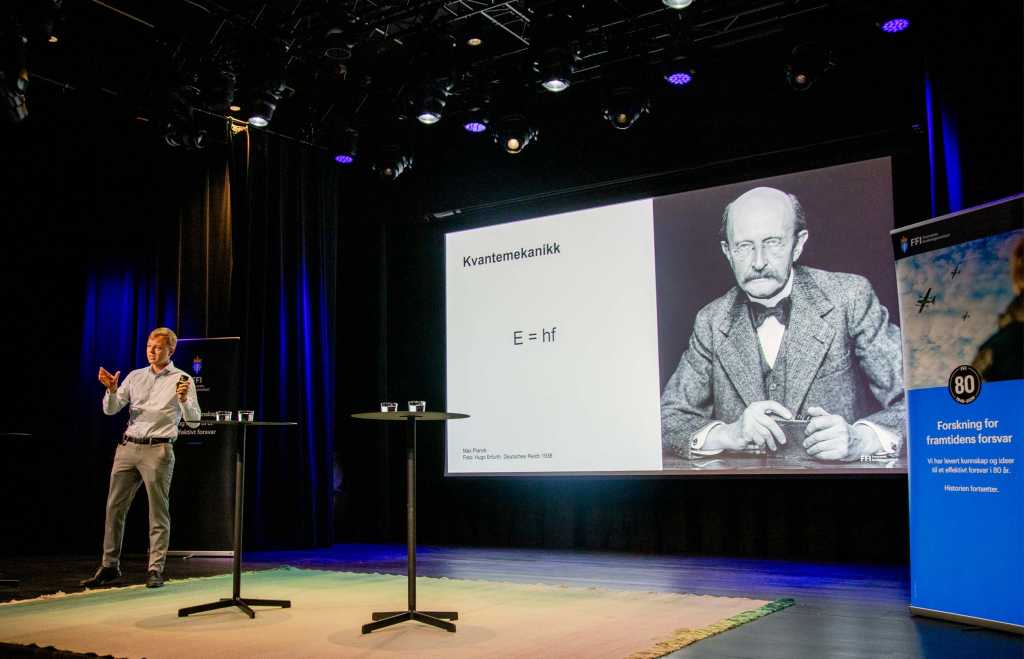 Forsker på scenen med et bilde av Max Planck i bakgrunnen.