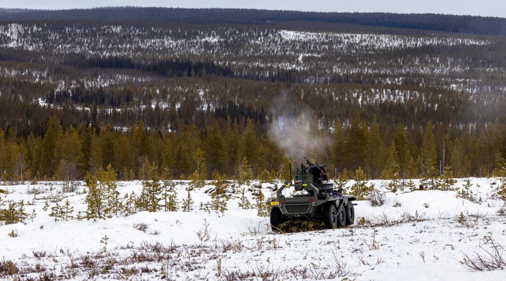 Ubemannet kjøretøy med våpenstasjon fyrer av skudd. UGV-en er står i åpent skogsterreng.