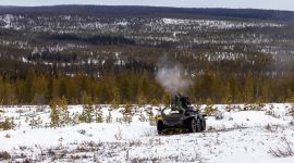 Ubemannet kjøretøy med våpenstasjon fyrer av skudd. UGV-en er står i åpent skogsterreng.