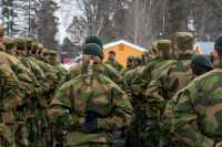 Soldater på oppstilling i grønn feltuniform. Alle står med ryggen til. I midten en kvinne med en lang flette.