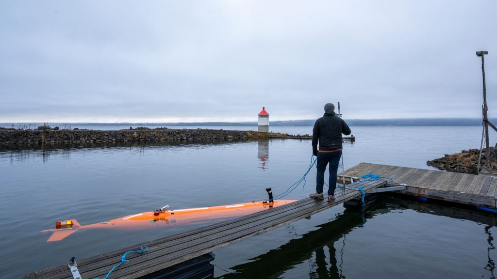 En  mann står i en småpåthavn på Gjøvik. I vannet nedenfor flyter en orange miniubåt. Mannen holder i et tau som er festet i ubåten.